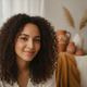 A close-up portrait of a smiling young woman with dark, curly hair, conveying happiness and trust. The background is softly b